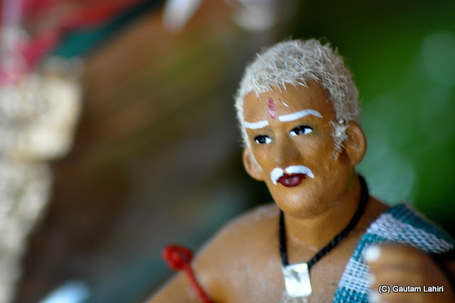 A fruit seller in close up made of clay stands barely 4 inches from ground stares at the customers at Krishnanagar, West Bengal, India by Gautam Lahiri