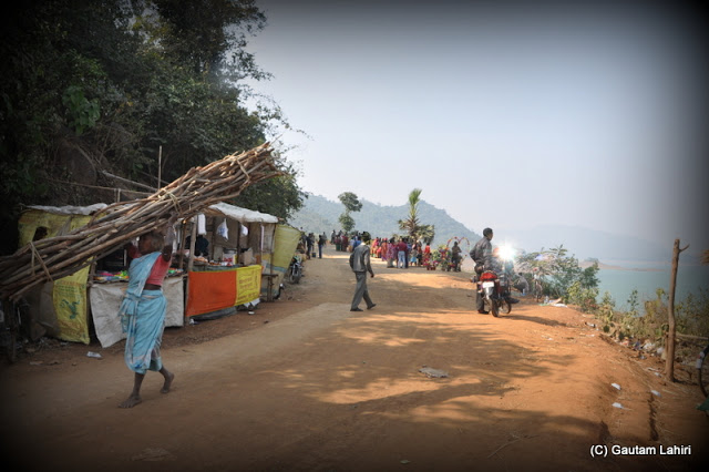 A village lady with wood on head skirt the hill road as we stare at the view  at Massanjore, Jharkhand, India by Gautam Lahiri