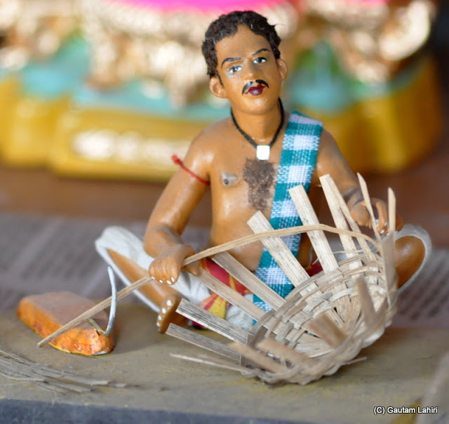 A basketmaker seen squatted as he adjusts the basket..you can also look at the cutter on the left which he uses to shape and shorten the bamboo strips.. all made of clay at Krishnanagar, West Bengal, India by Gautam Lahiri