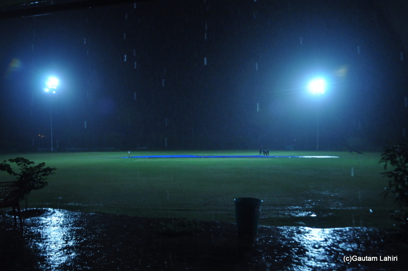 The floodlights glow under the driving rain on a cricket field by Gautam Lahiri