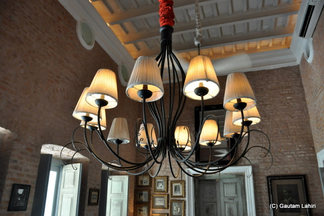 A chandelier puts in a mild glow around the dining room along with the daylight filtering through the glass doors at Bawali Rajbari, Kolkata, West Bengal, India by Gautam Lahiri