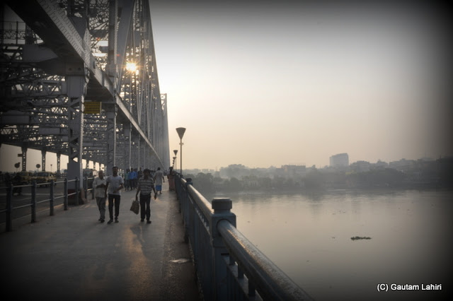 The smoke and fog enveloped the city limits, while the Howrah bridge stood tall and gallant ushers the sun and the new day  at Kolkata, West Bengal, India by Gautam Lahiri