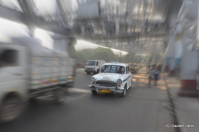 The Calcutta 'Taxi' the good old Ambassador proudly drives over the Howrah bridge. Kolkata is incomplete without a ride in this car at Kolkata, West Bengal, India by Gautam Lahiri