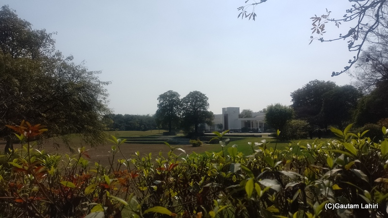 The Tree Auditorium reveals a glimpse of its exterior through the manicured bushes beneath a blue sky by gautam lahiri