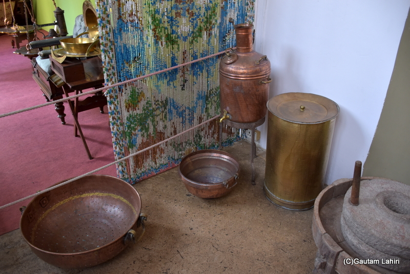 The Maharaja's queen of Naulakha Palace in Gondal personally tended to the kitchen. Every item you observe here is crafted from brass or copper, chosen for their health benefits. A copper water decanter and a perforated tumbler rest near a curtain, adjacent to a stone grinder. All processes are manual, devoid of any chemicals or machinery by gautam lahiri