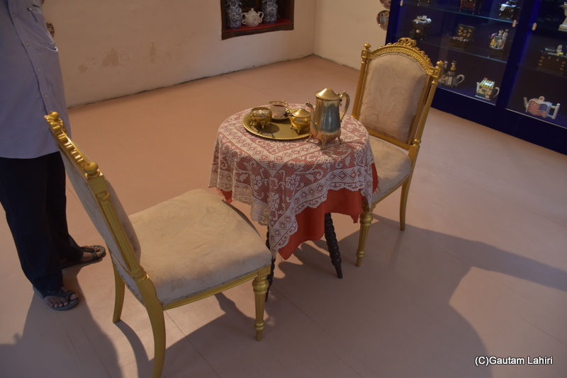 A round table crafted from mahogany wood, decorated with a brass tea set atop a lace-embroidered table cover, and complemented by gold-plated wooden chairs with plush cushions, reflects the regal lifestyle at Naulakha Palace in Gondal by gautam lahiri  