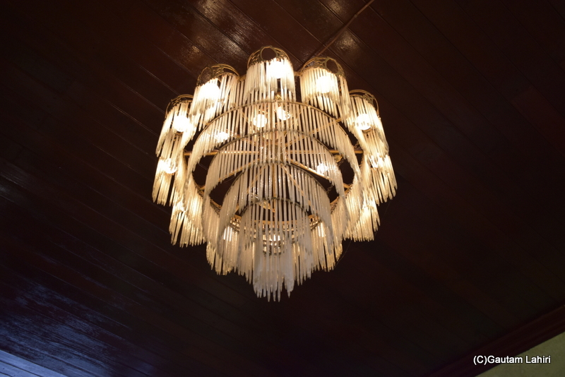A fringe chandelier hung from the wooden ceiling, adorned with numerous frosted glass rods, arranged in several concentric patterns, cast a dispersed light throughout the room at Naulakha Palace, Gondal by gautam lahiri