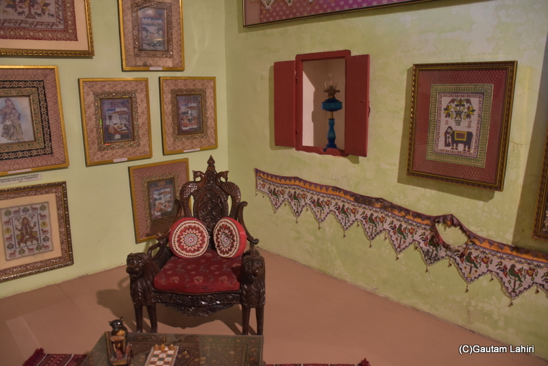 Handmade embroidered images of mythical figures and animals, along with gods and goddesses, encircle a majestic lion-carved wooden chair positioned centrally. In front, an ancient "Pachisi" game is displayed on a glass-topped low mahogany table at Naulakha Palace, Gondal by gautam lahiri
