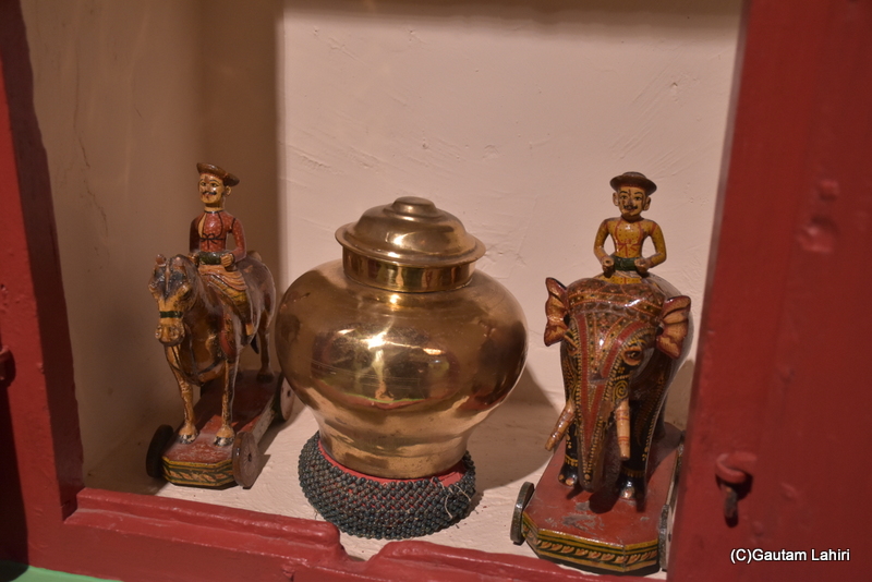 A gleaming brass tumbler, flanked by two ornately carved wooden Royal soldiers mounted on an elephant and a horse, seemed to gaze at us through the glass, Note the unique caps the soldiers wore were of the Royal family at Naulakha Palace in Gondal by gautam lahiri